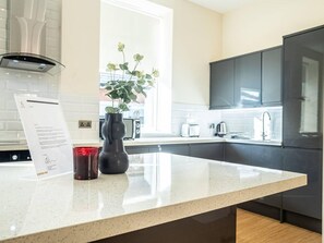 Une cuisine moderne avec un plan de travail blanc, des meubles de couleur sombre, une fenêtre et un vase contenant des plantes vertes.