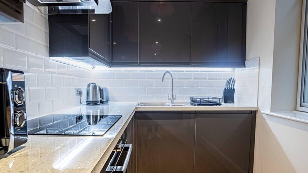 A modern kitchen with a built-in stove, a sink, and dark cabinetry. - Contemporary One Bedroom Flat by Sojo Stay (Ipswich)