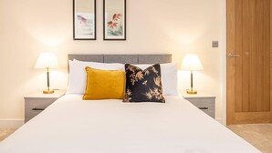 A hotel room with a large bed, two bedside lamps, a wooden door, and two framed pictures on the wall. - Contemporary One Bedroom Flat by Sojo Stay (Ipswich)