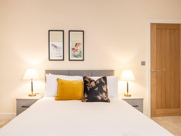 A hotel room with a large bed, two bedside lamps, a wooden door, and two framed pictures on the wall. - Contemporary One Bedroom Flat by Sojo Stay (Ipswich)