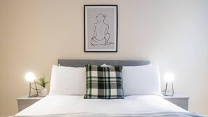 A neatly made bed with a plaid pillow, two bedside lamps, and a framed artwork on the wall. - Contemporary One Bedroom Flat by Sojo Stay (Ipswich)