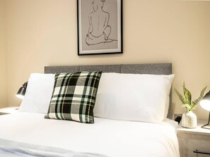 A neatly made bed with white linens, a grey headboard, and a green plaid pillow. A framed line drawing hangs on the wall above the bed. - Contemporary One Bedroom Flat by Sojo Stay (Ipswich)
