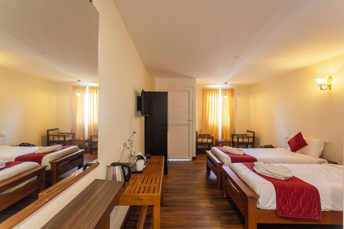 A hotel room with three beds, a wooden bench, a table, a TV, and a door.