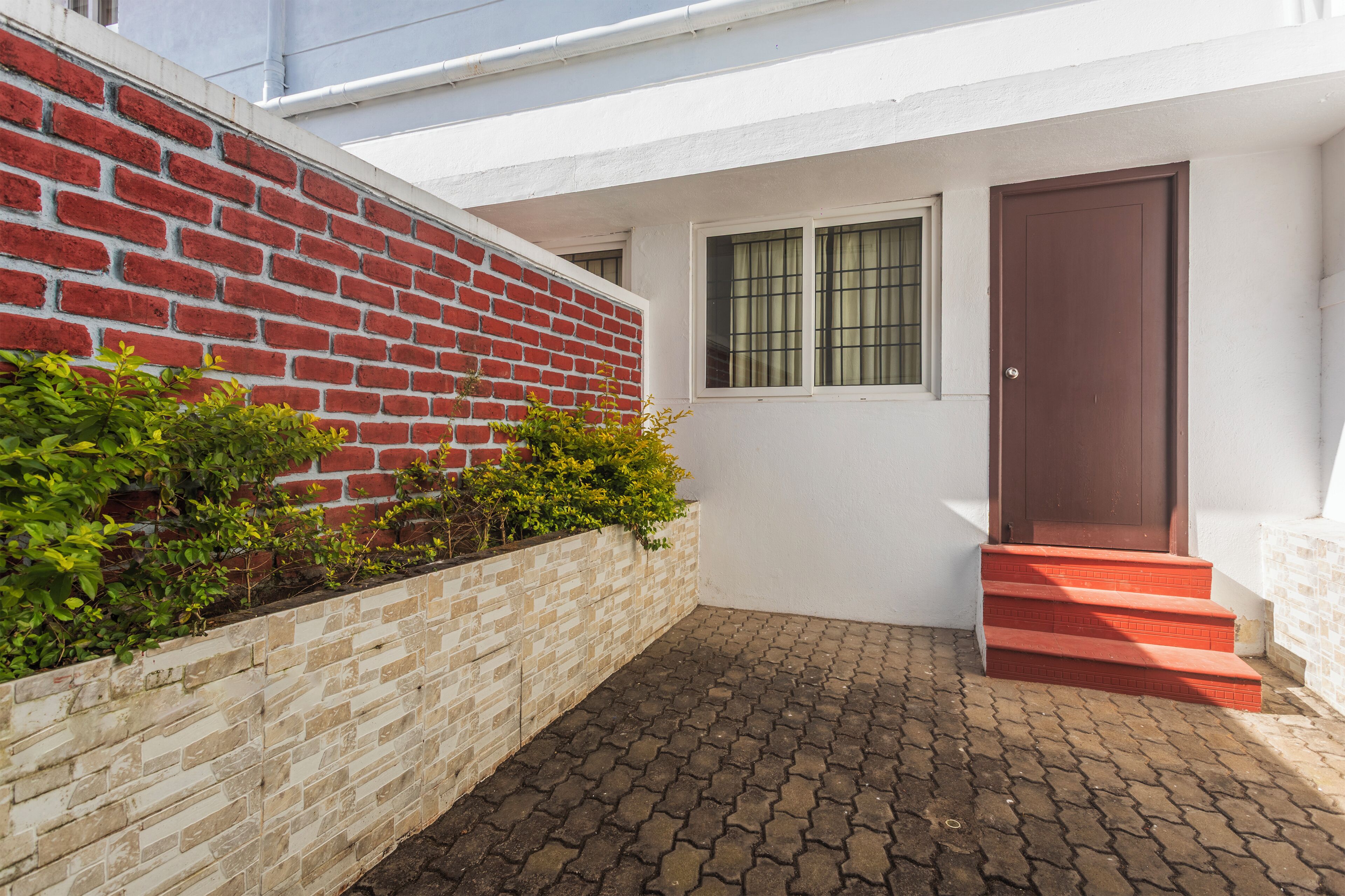 A house with a red brick wall, a white exterior, a window with green curtains, and a brown door.