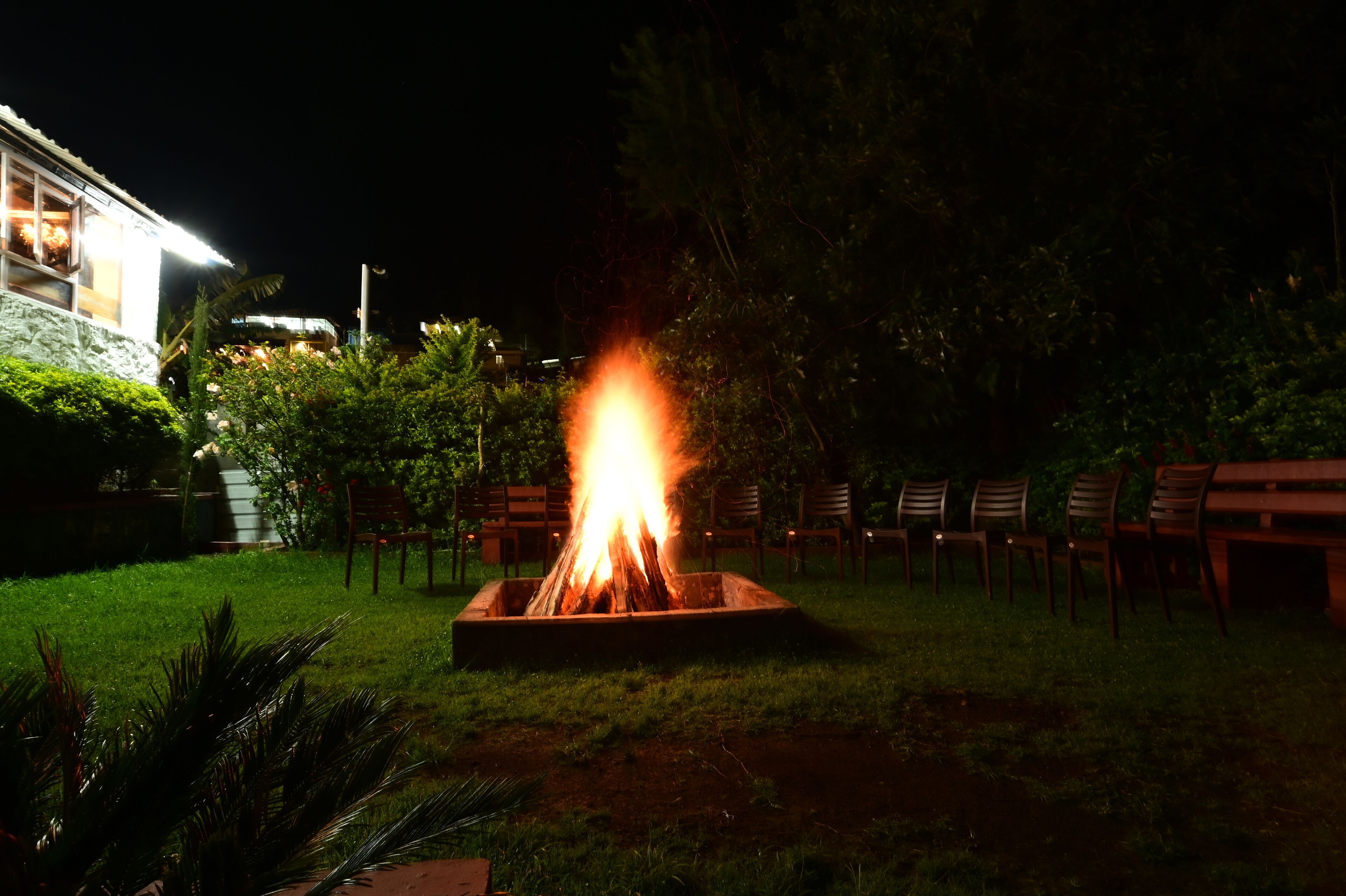A nighttime outdoor fire feature surrounded by chairs and a building in the background.