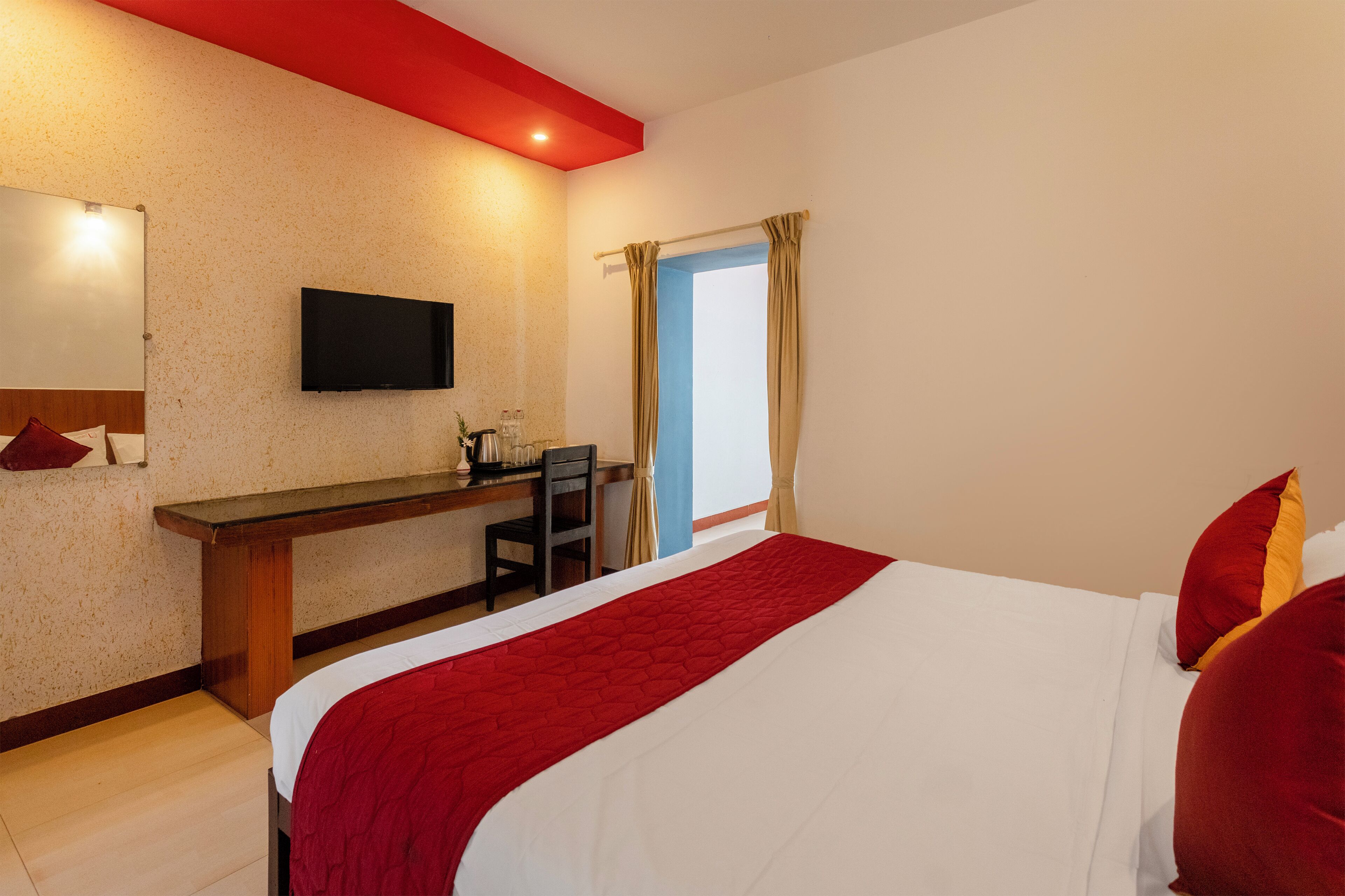 A hotel room with a bed, a desk, a chair, a television, and a window with curtains.