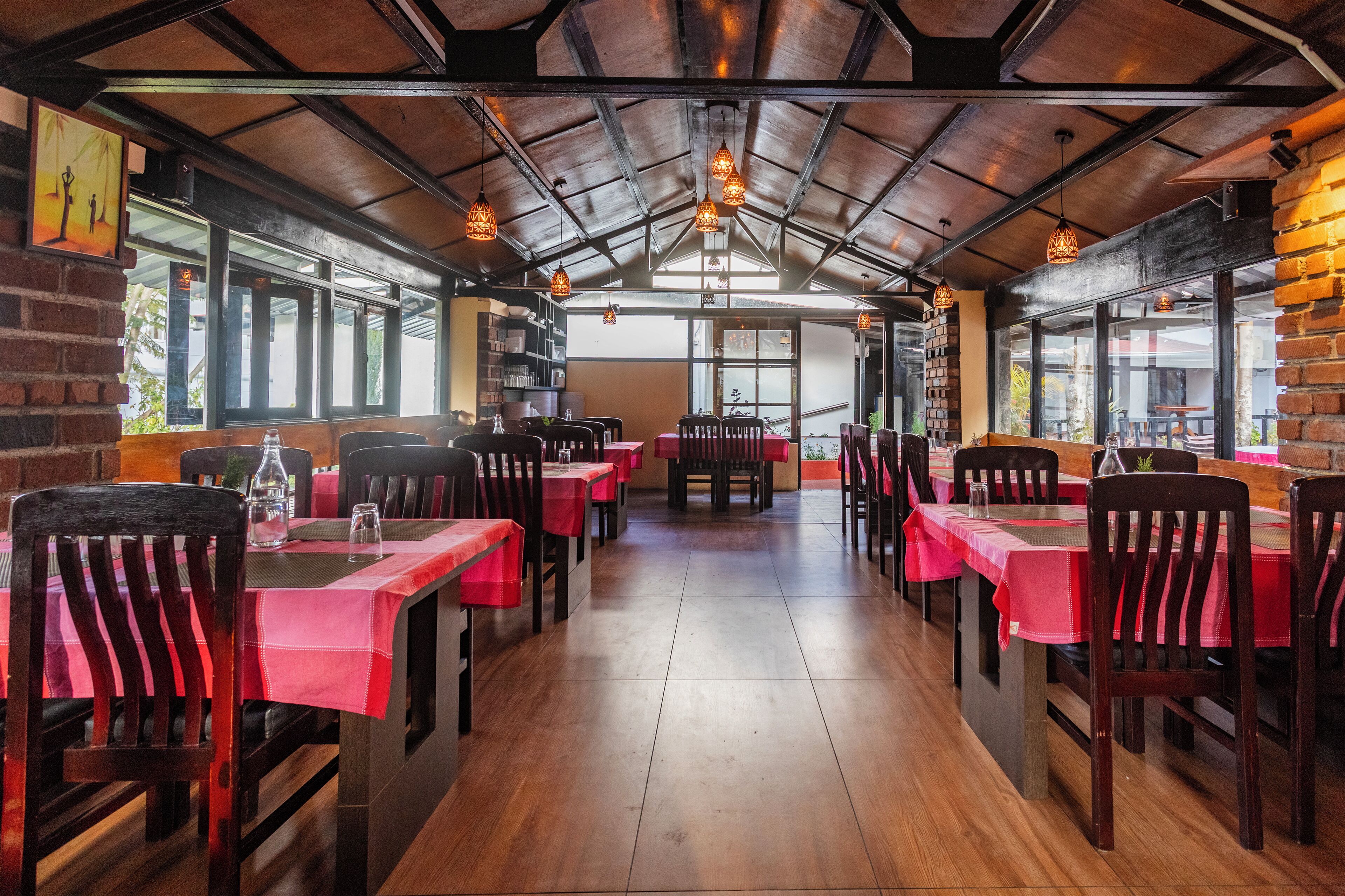 Interior de restaurante con mesas de madera, manteles rojos, lámparas colgantes y paredes de ladrillo.