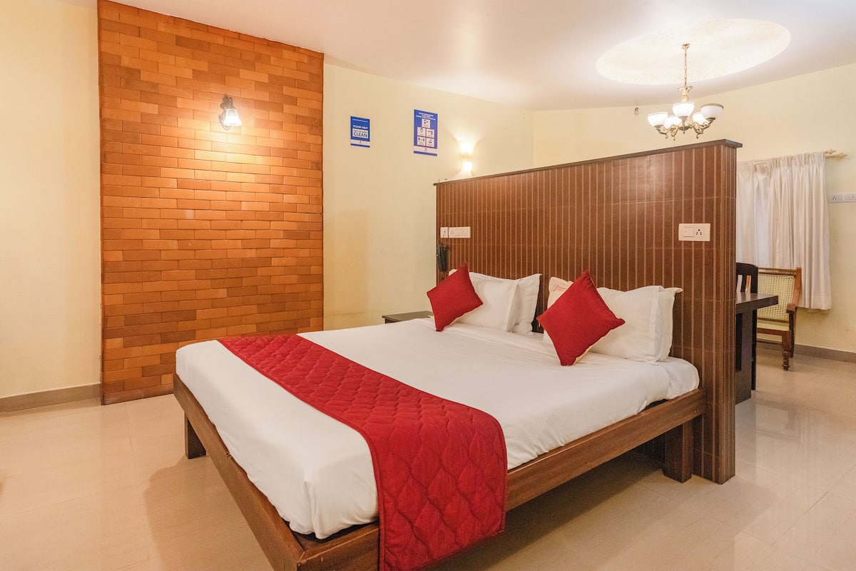 A hotel room with a wooden bed, a red quilted bedspread, a brick accent wall, and a chandelier.