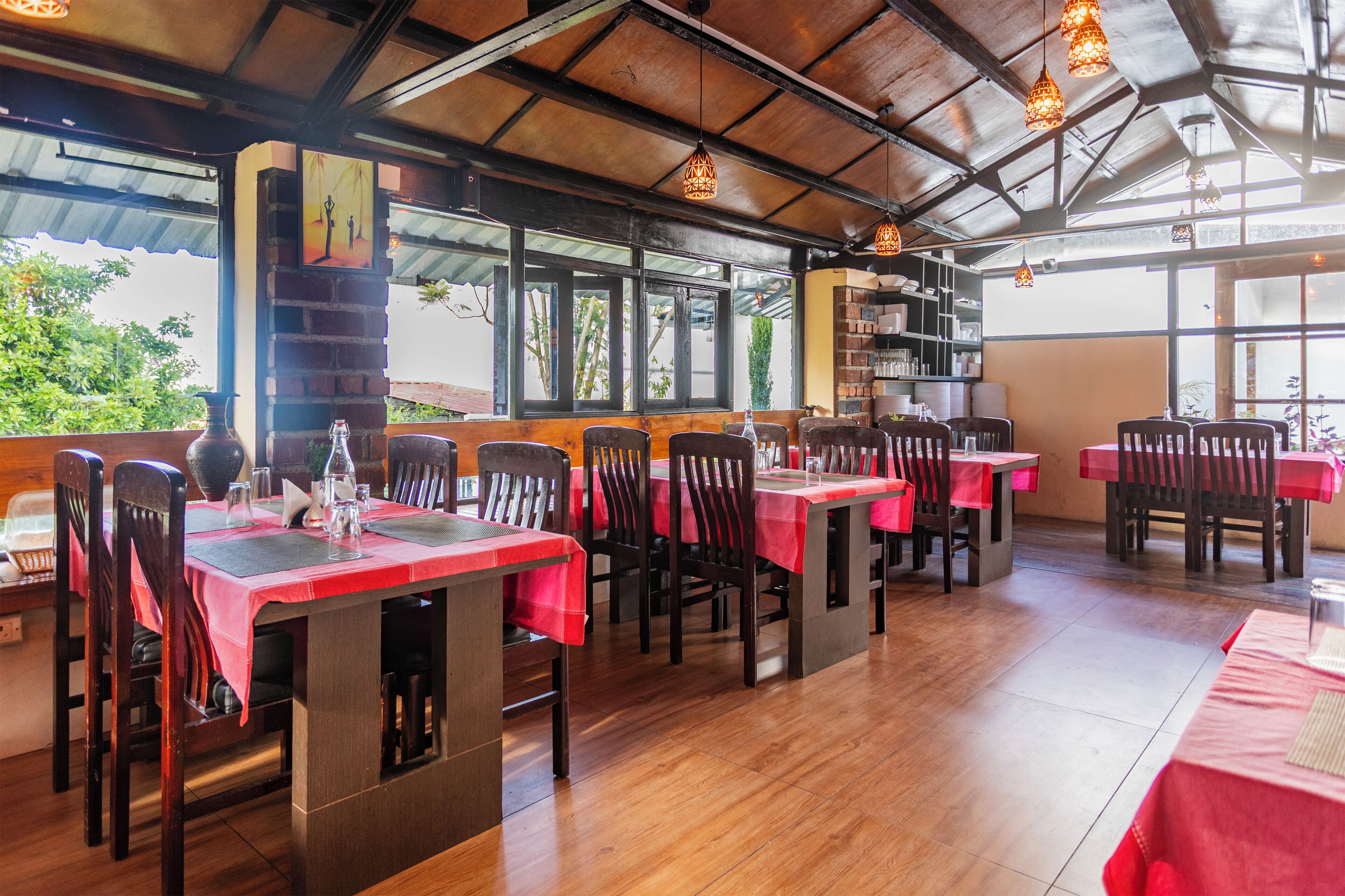 A restaurant with wooden tables and chairs, red tablecloths, and hanging pendant lights.