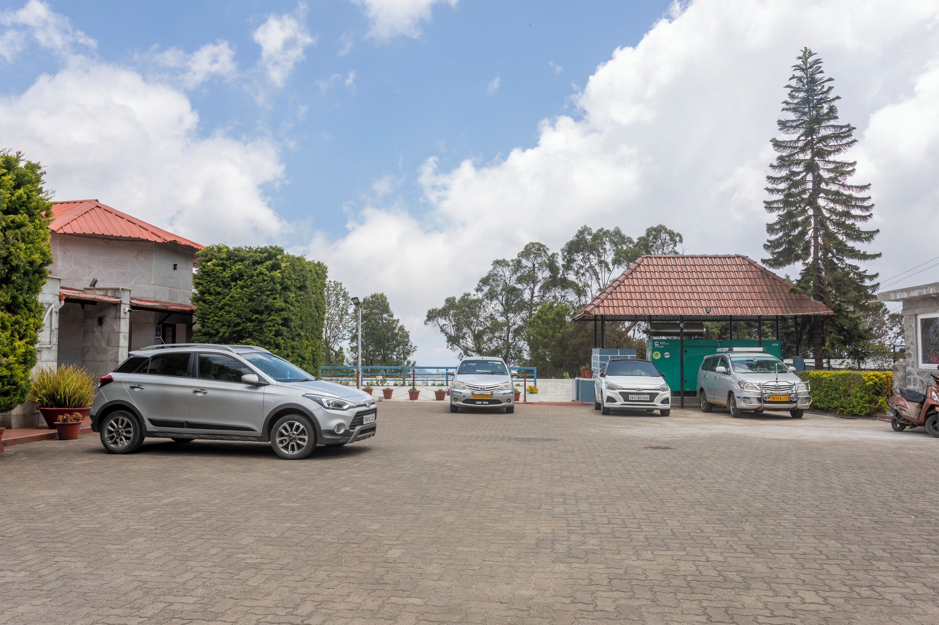 A parking area with several cars, a building with a red roof, and a tall tree.