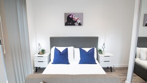 Une chambre d’hôtel moderne avec un grand lit, deux tables de chevet, une petite table et une œuvre d’art accrochée au mur.