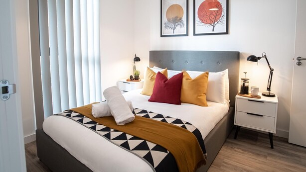 A modern bedroom with a large bed, a bedside table, a nightstand, and two wall-mounted lamps. - One Super King Bedroom Kelham Island by Belvilla (Sheffield)