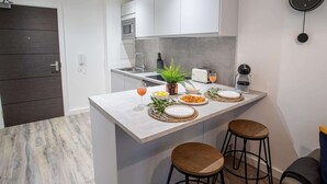 A modern kitchen with white cabinetry, a central island with stools, a microwave, and a clock on the wall. - One Super King Bedroom Kelham Island by Belvilla (Sheffield)