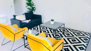 A modern living room with a dark blue sofa, two yellow armchairs, a coffee table, and a patterned rug. - Peak District One King Bedroom Haven by Belvilla (Sheffield)
