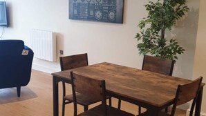 Un comedor con una mesa de madera y cuatro sillas, una silla azul, una planta en maceta y una obra de arte colgada en la pared.