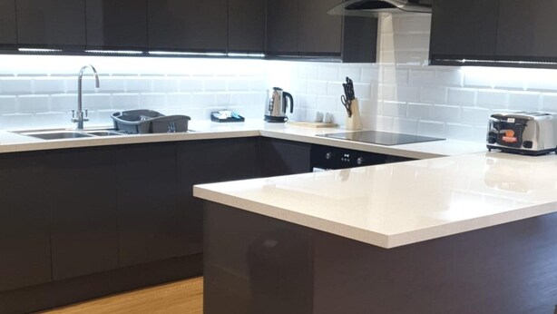 Una cocina moderna con una isla central, armarios oscuros y encimera blanca.