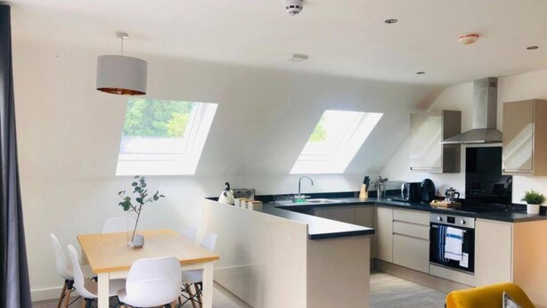 A modern kitchen with a central island, skylights, and a dining area with yellow chairs.