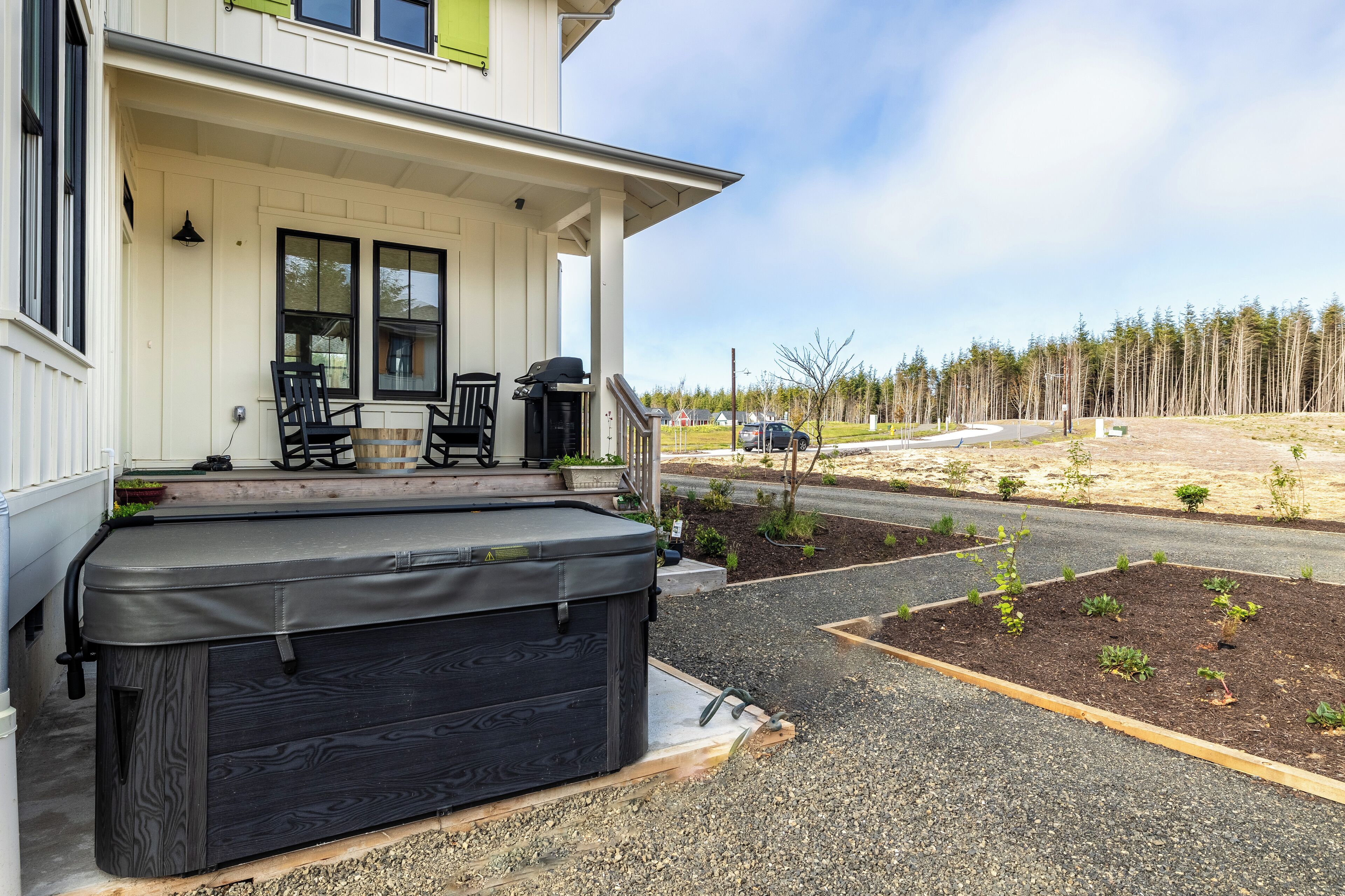 Een huis met een overdekte veranda, een hottub en een tuin met jonge planten.