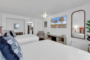 Ein Hotelzimmer mit zwei Betten, einem Schreibtisch, einem Stuhl, einem großen Spiegel und Bildern an den Wänden.