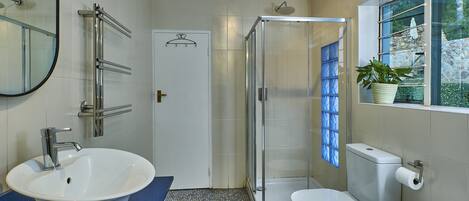 A bathroom with a white sink, a glass shower enclosure, a toilet, and a window with a view of greenery.