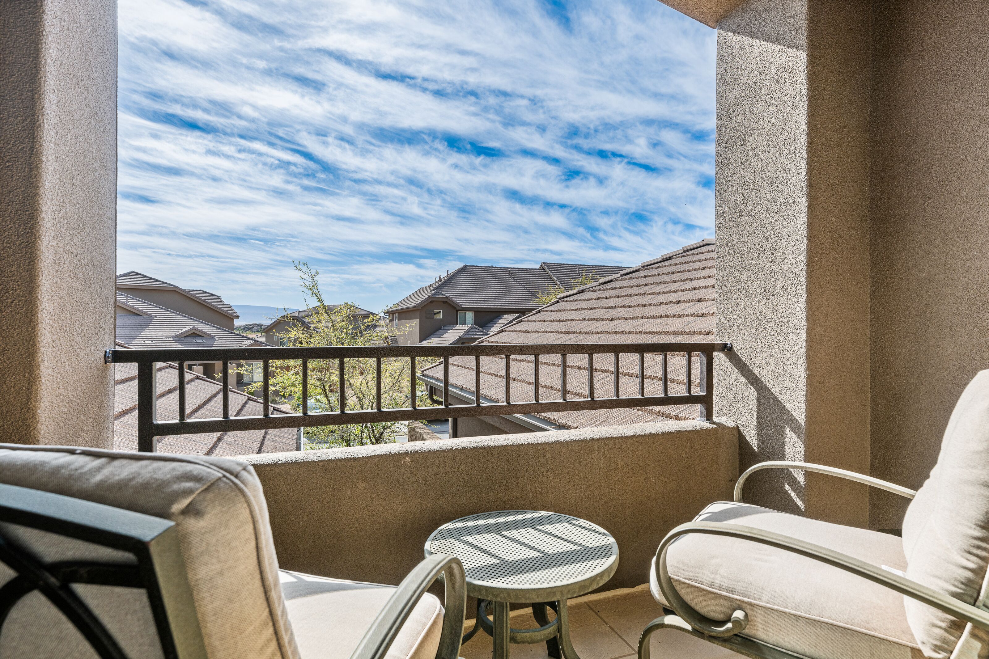 A balcony with a view of neighboring houses, a round table, and two chairs.