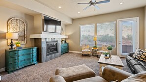 A living room with a fireplace, a ceiling fan, and a large window with blinds. - Zion's Edge: Two Pools and Hot Tubs, Clubhouse Gym (Washington)