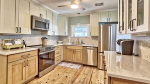 A kitchen with light wood cabinets, stainless steel appliances, a wooden floor, and a ceiling fan.