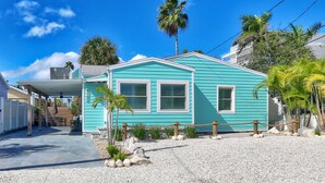 A turquoise house with a covered patio, palm trees, and a gravel driveway.