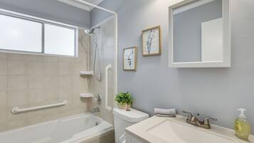 Une salle de bain avec une baignoire, un lavabo, des toilettes et une douche. Il y a des tableaux encadrés au mur et une plante en pot.