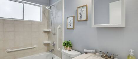 A bathroom with a bathtub, a sink, a toilet, and a shower. There are framed pictures on the wall and a potted plant.