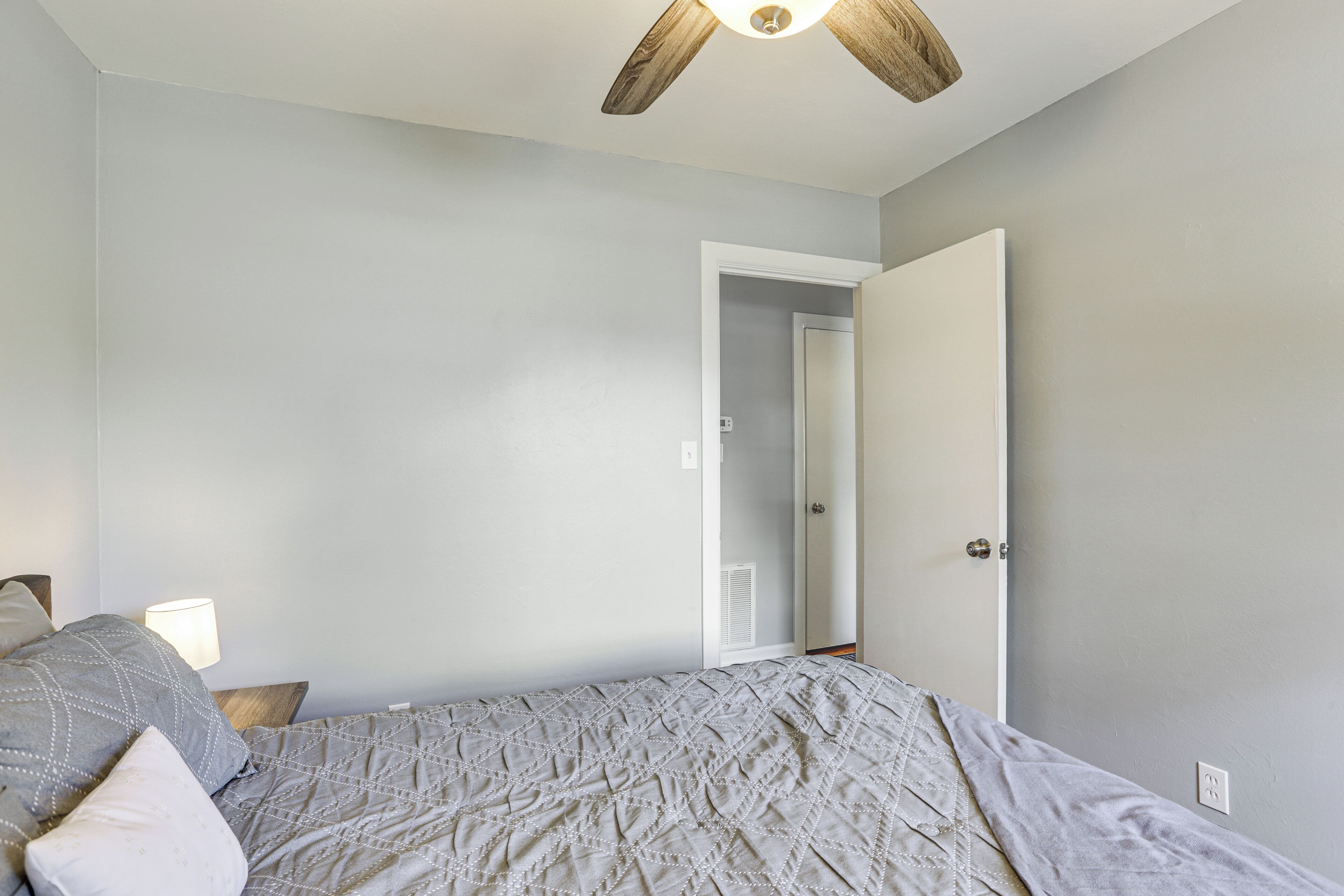 A bedroom with a bed, a ceiling fan, a door, and a nightstand with a lamp.