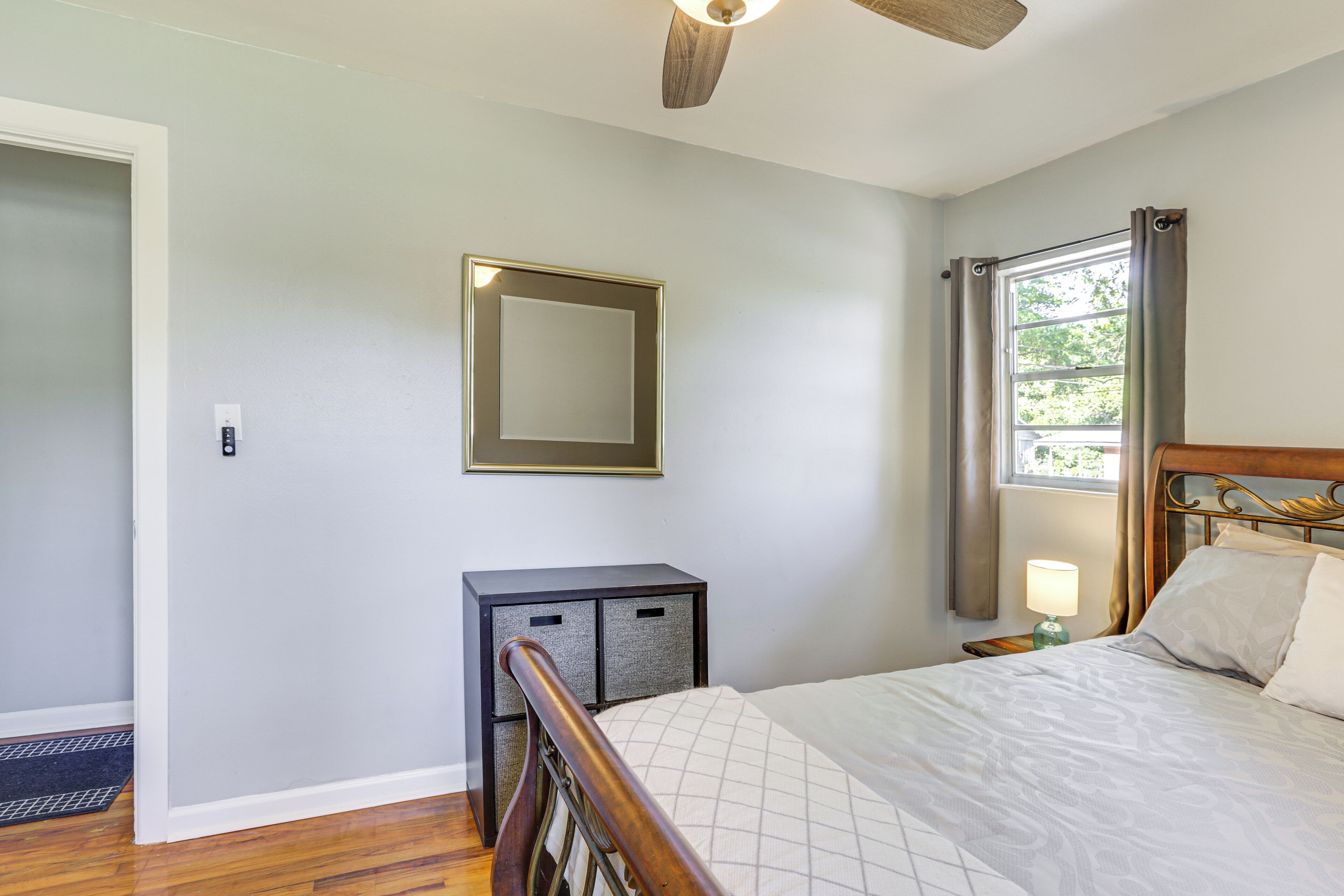 A bedroom with a bed, a nightstand, a dresser, a mirror, and a window with curtains.