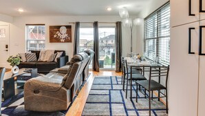 A modern living room with a sofa, a dining table with chairs, and a view through a glass door. - Modern Elizabeth Apartment ~ 1 Mi to Train Station (Elizabeth)