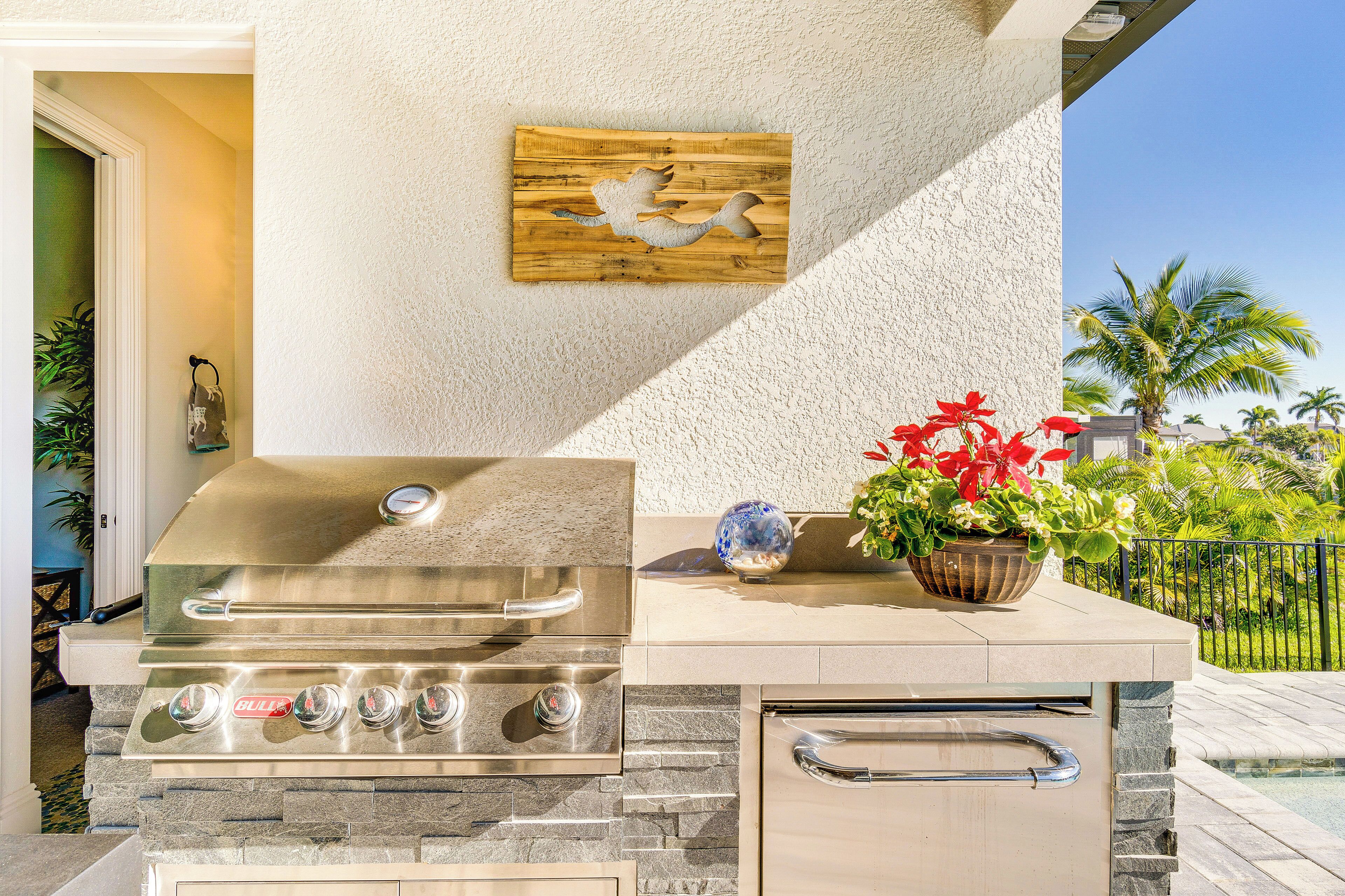 An outdoor kitchen with a stainless steel grill, stone accents, and a decorative fish wall art piece.