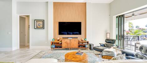 A spacious living room with a large flat-screen TV, comfortable seating, and a ceiling fan.