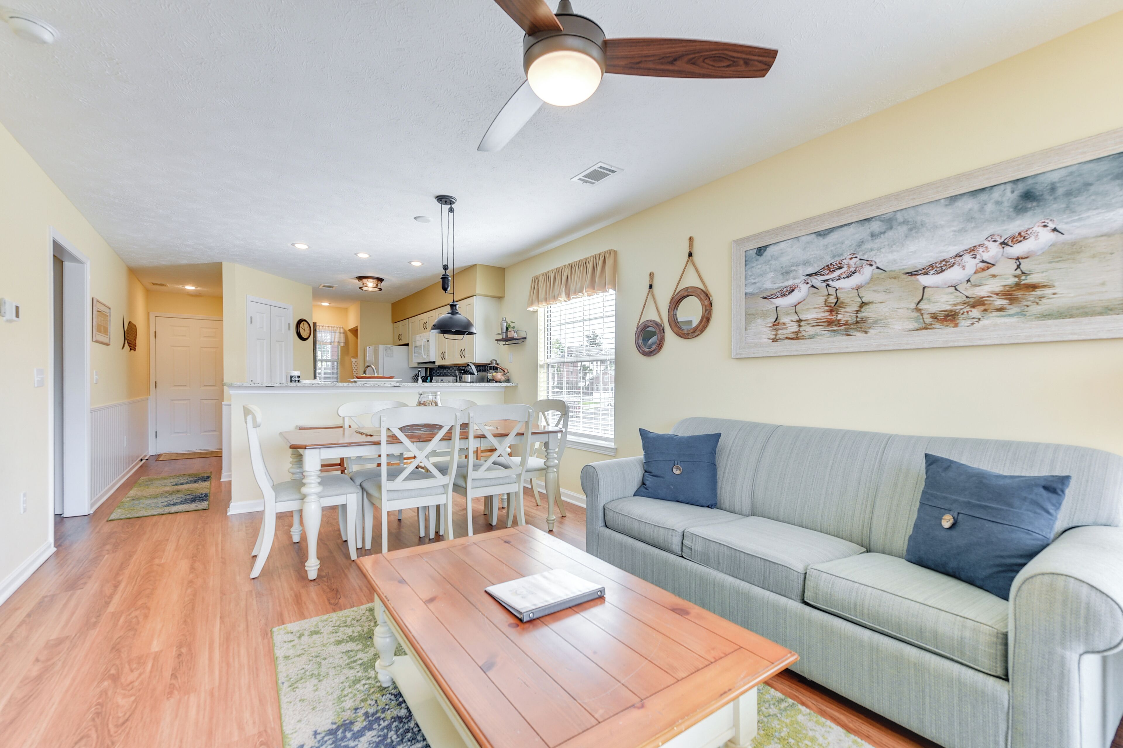 A living room with a gray sofa, a wooden coffee table, and a dining area with white chairs and a table.