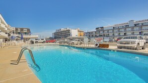 Ein Schwimmbecken mit einer Metallleiter, umzäunt, mit Gebäuden im Hintergrund.