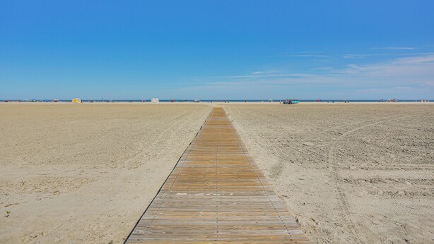 Eine lange Holzpromenade, die zu einem Strand mit blauem Himmel führt.