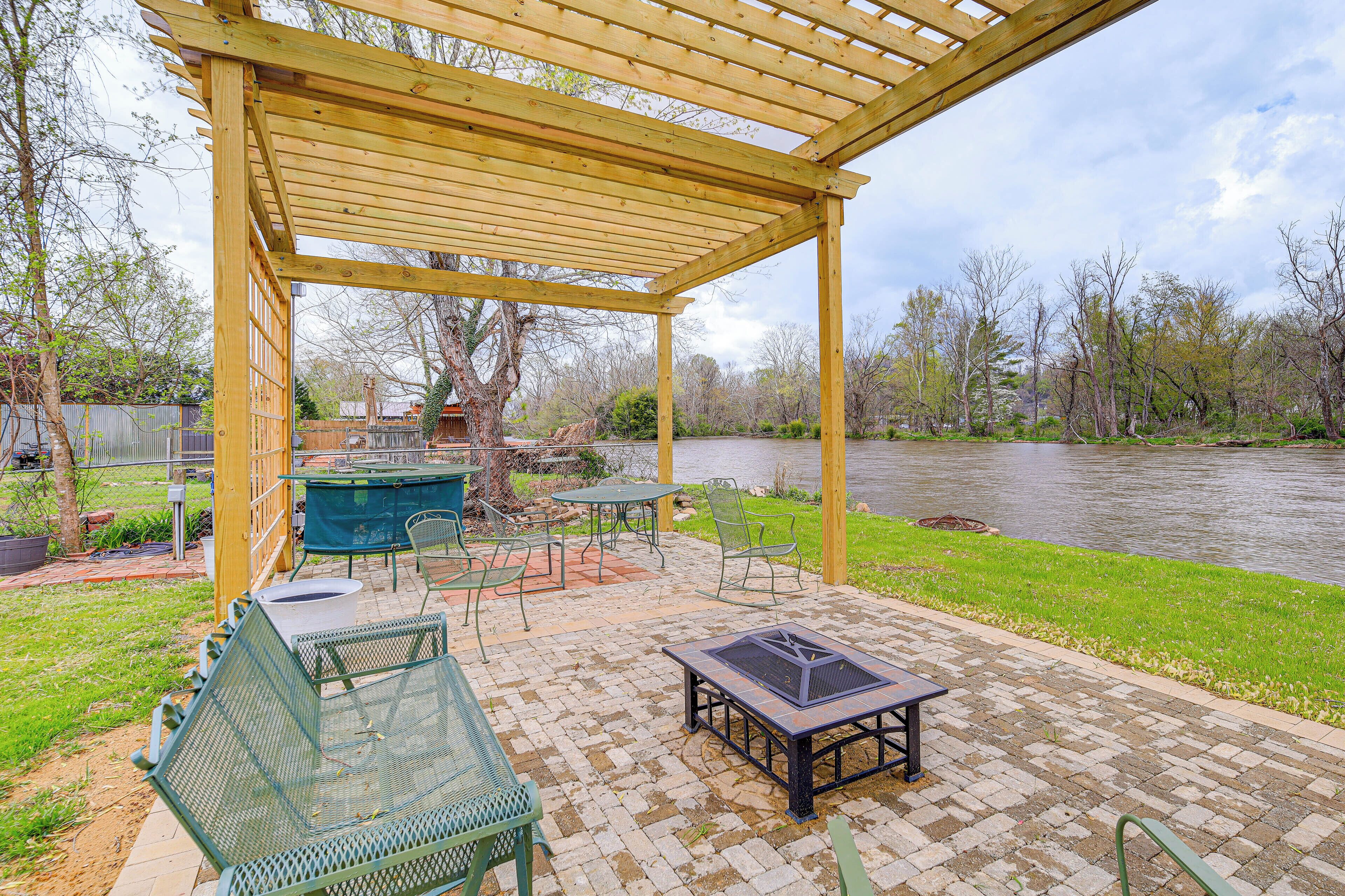 Ein überdachter Patio-Bereich mit Sitzgelegenheiten im Freien, einer Feuerstelle und Blick auf einen Fluss.