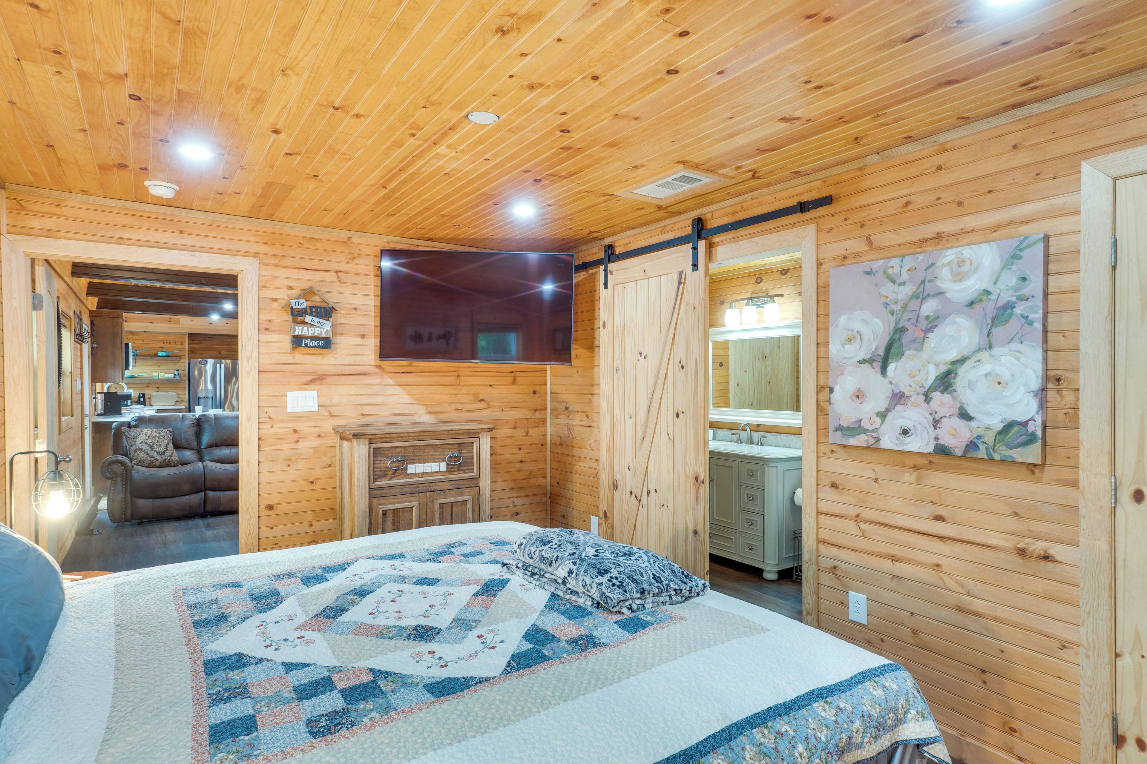 Une chambre à coucher aménagée dans une cabane en bois, avec un lit, une commode, un tableau et une porte coulissante donnant sur une salle de bain.