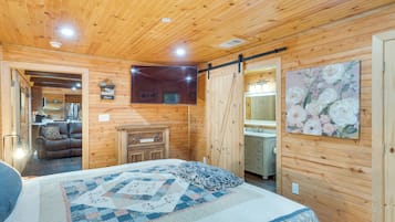 Une chambre à coucher aménagée dans une cabane en bois, avec un lit, une commode, un tableau et une porte coulissante donnant sur une salle de bain.