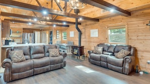 A cozy cabin interior with a wooden interior, two leather sofas, a dining area, and a kitchen.