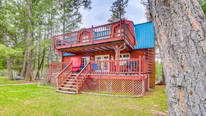 A cabin with a wooden deck, a staircase, and a blue exterior wall. - Secluded Bigfork Cabin w/ Yard & Fire Pit! (Bigfork)