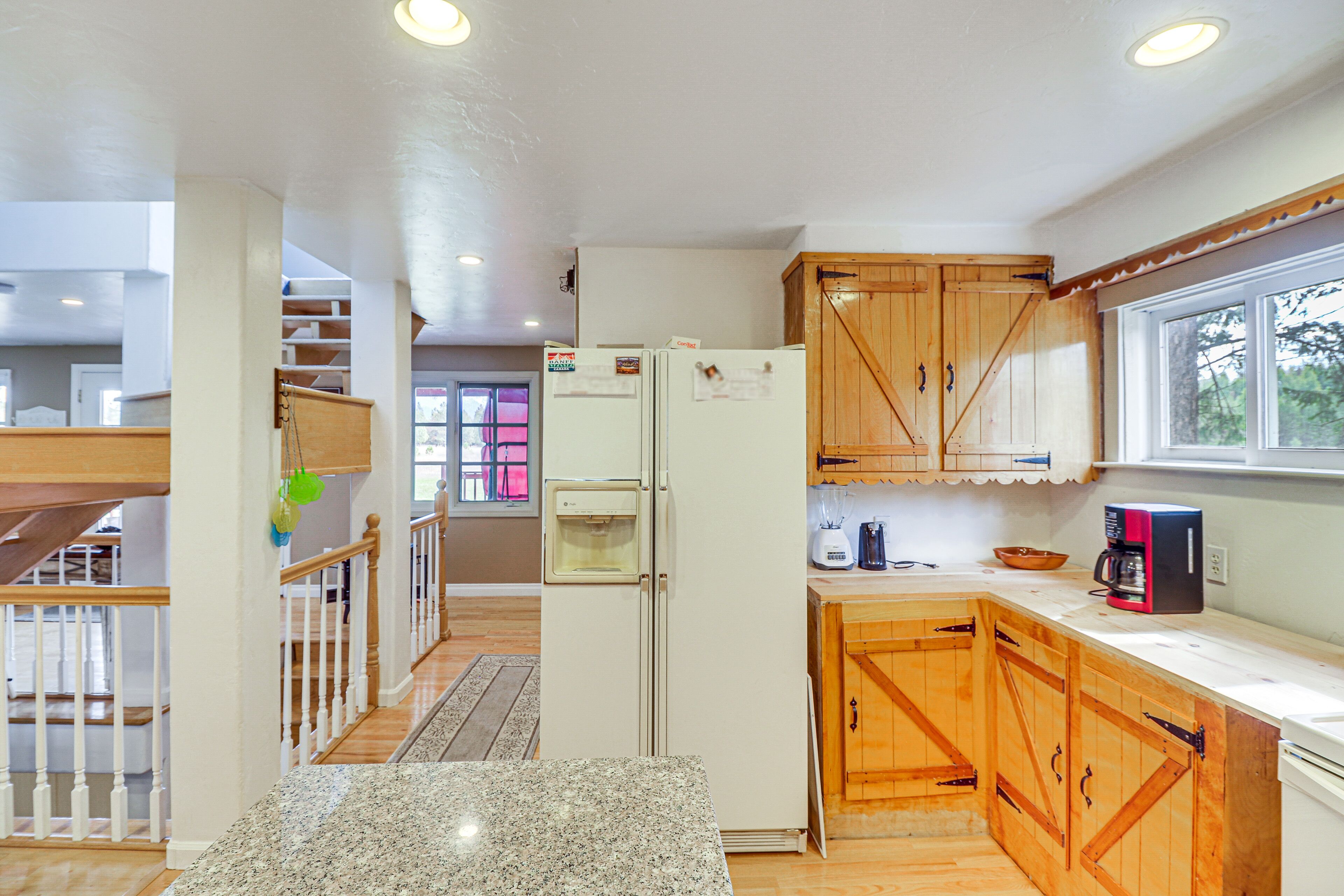 A kitchen with wooden cabinets, a refrigerator, a coffee maker, and a window.