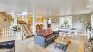 A spacious living area with a sofa, coffee table, and dining table. A staircase leads to an upper level with a kitchen and dining area. - Secluded Bigfork Cabin w/ Yard & Fire Pit! (Bigfork)