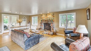 A spacious living room with a stone fireplace, a dining area, and a seating area with sofas and a coffee table. - Secluded Bigfork Cabin w/ Yard & Fire Pit! (Bigfork)