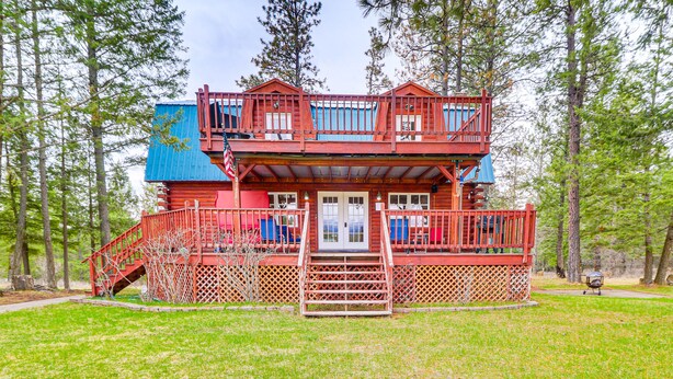 A two-story log cabin with a red exterior, a front porch, and a staircase leading to the upper level. - Secluded Bigfork Cabin w/ Yard & Fire Pit! (Bigfork)
