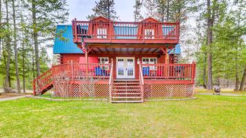 A two-story log cabin with a red exterior, a front porch, and a staircase leading to the upper level.