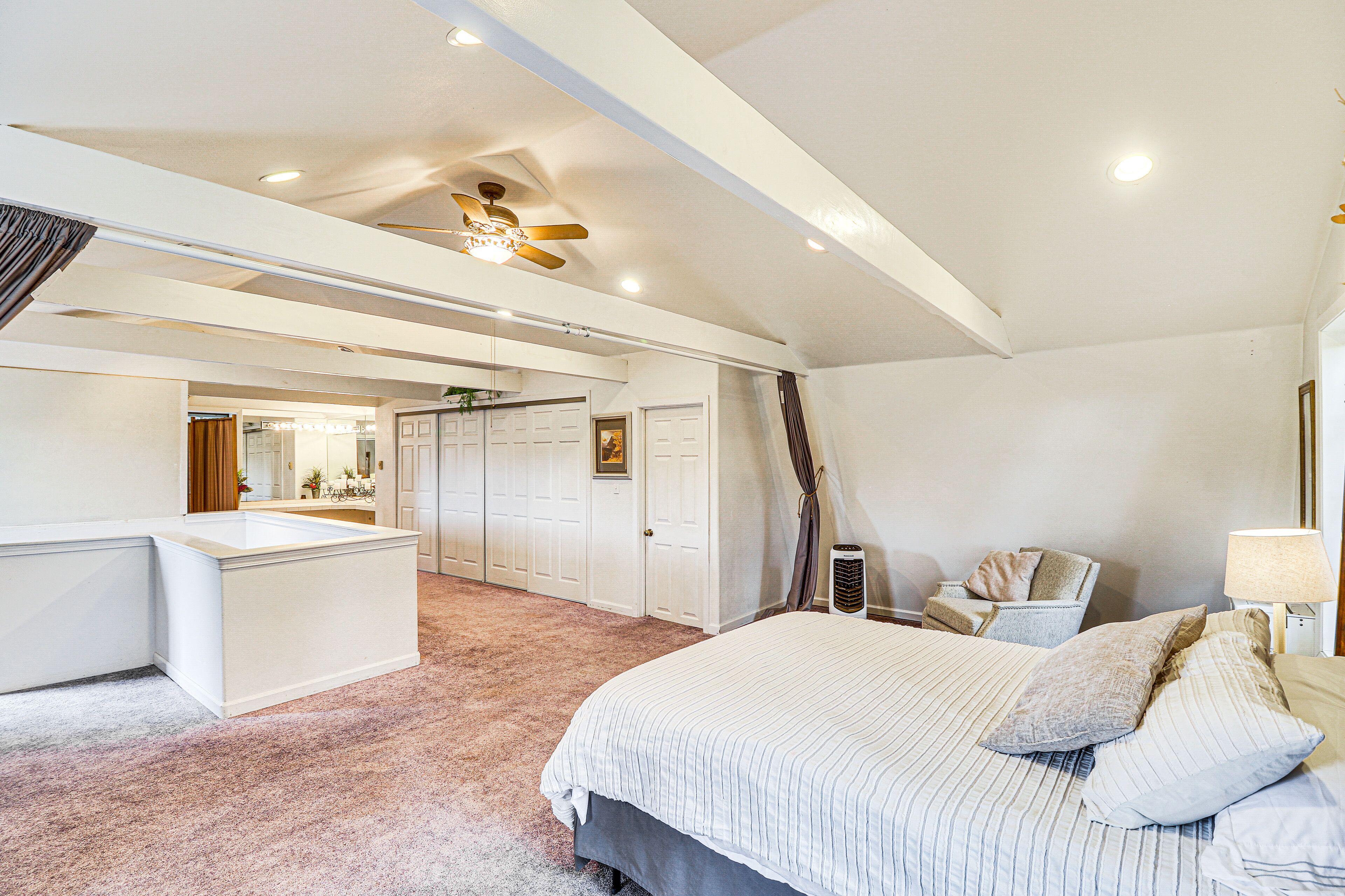 Une chambre spacieuse avec un grand lit, un bureau et une chaise. Elle est équipée d’un ventilateur de plafond et de luminaires encastrés.