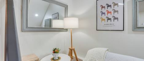 Een keurig opgemaakte slaapkamer met een grote spiegel, een lijst met een afbeelding van Zweedse paarden, een bedlamp, een klein tafeltje met een plant en een gezellig bed met een geborduurd plaid.